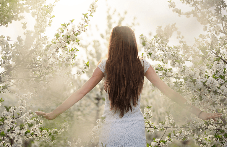 Woman in a white dress in a dreamlike setting among apple blossoms. Amplifying the power of manifestation.